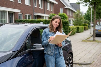 Jeune femme souriante à côté d'une voiture électrique dans un quartier calme